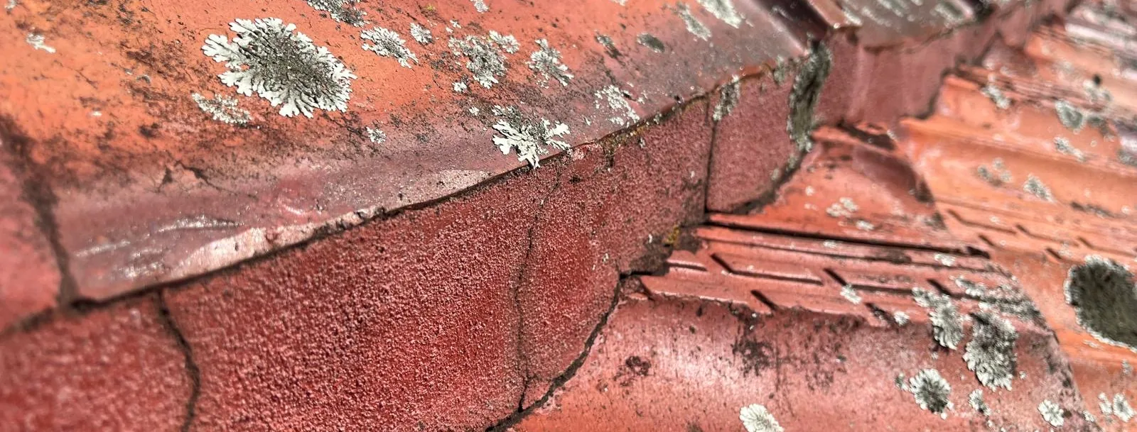 Broken ridge tiles and perished pointing on a terracotta roof
