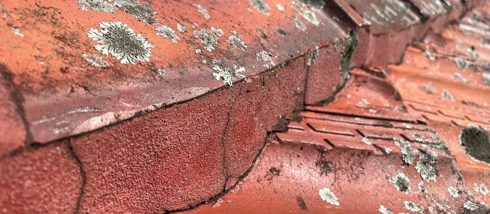 Broken ridge tiles and perished pointing on a terracotta roof