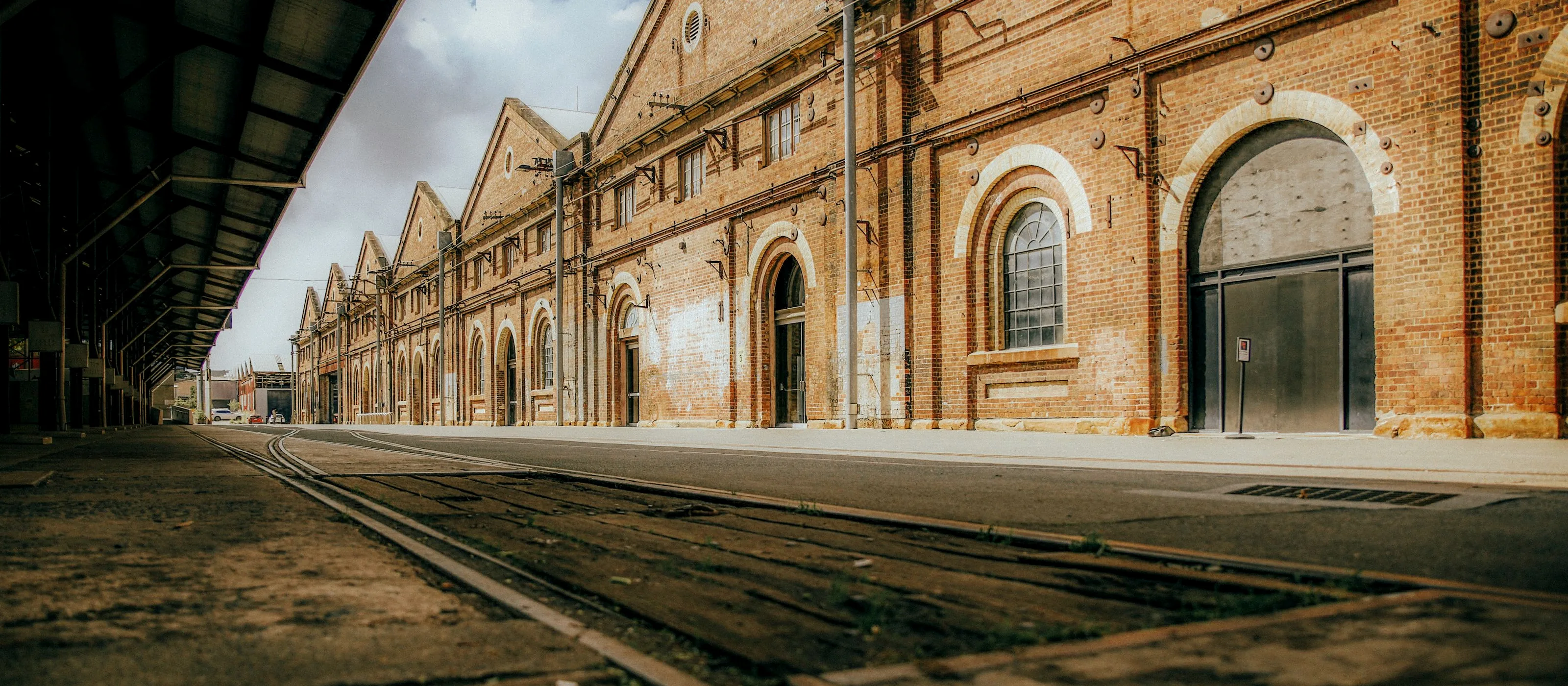 Long brick industrial building with arched bays alongside disused rail tracks
