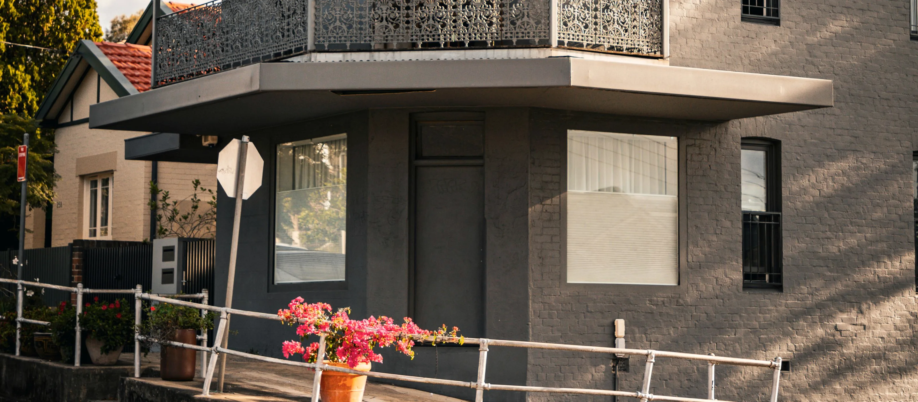 Older Sydney corner building with an iron balustrade, deep verandah and terracotta roof behind