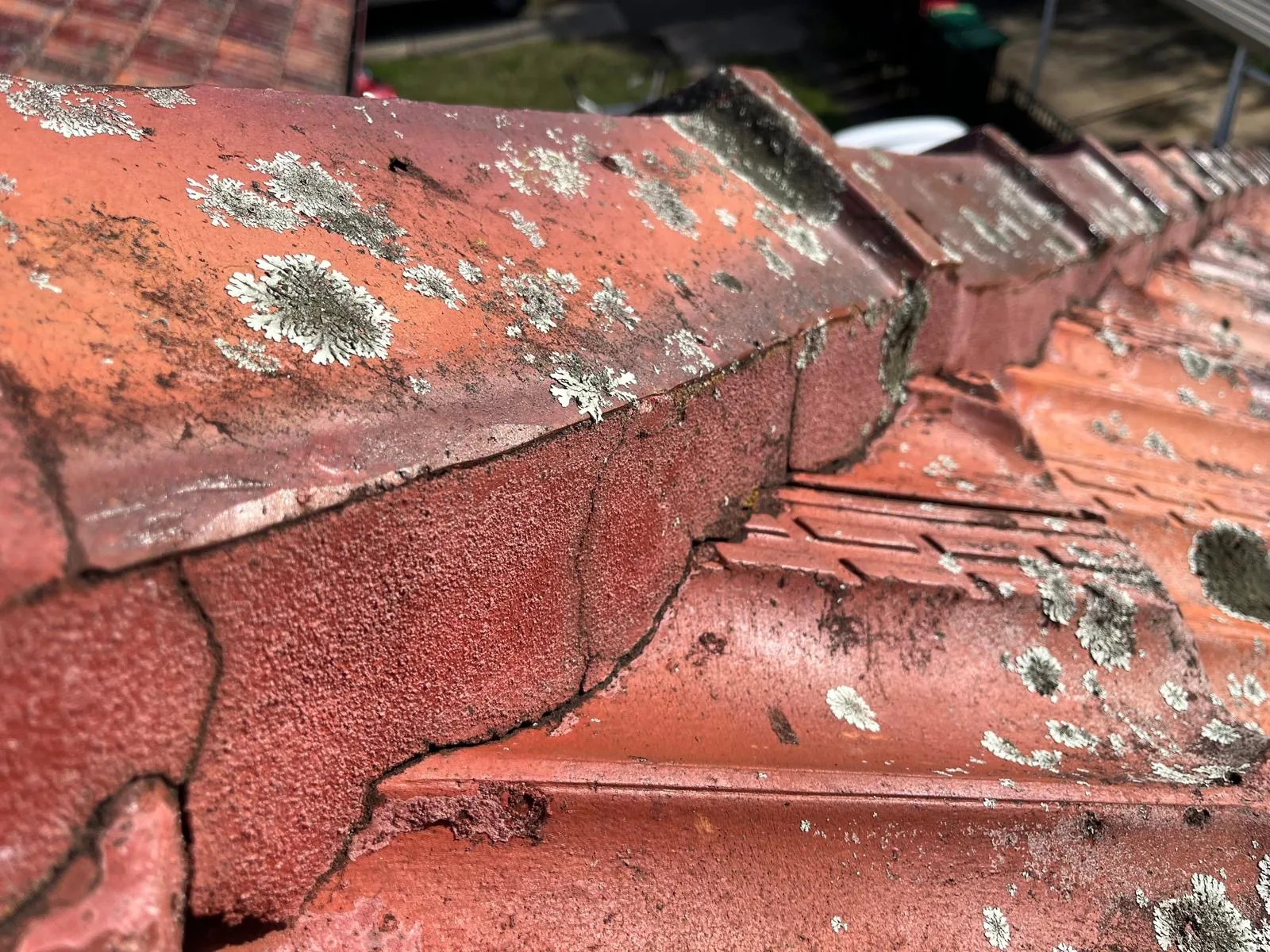 Broken ridge tiles and failed pointing on a terracotta roof