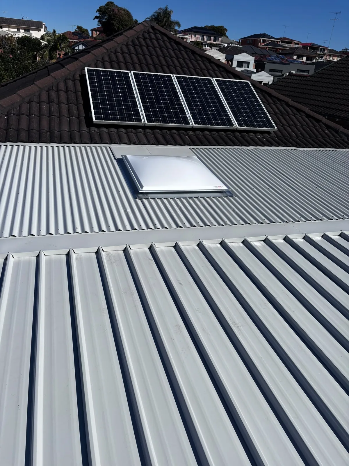 Metal roof with skylight beside an original tile roof and solar panels